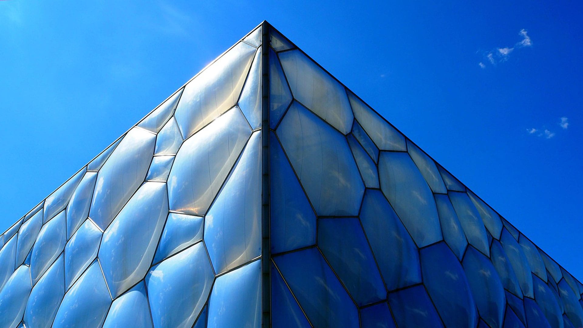 A striking close-up of the geometric facade of the Water Cube in Beijing, reflecting the vibrant blue sky