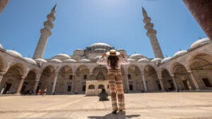 Woman with a sunhat standing in the courtyard of the Blue Mosque, Istanbul, gazing up at the beautiful domes and minarets against a clear blue sky.