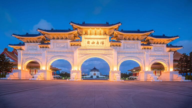 The illuminated grand gate of Chiang Kai-shek Memorial Hall with intricate designs and a clear blue evening sky