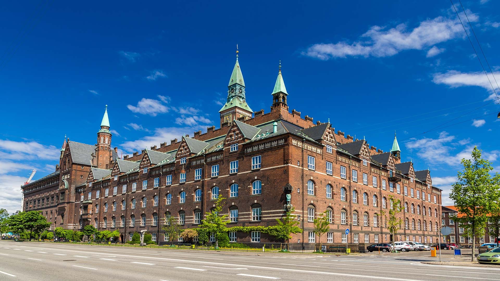 Copenhagen City Hall, a historic red-brick building with green rooftops and towers against a clear blue sky.