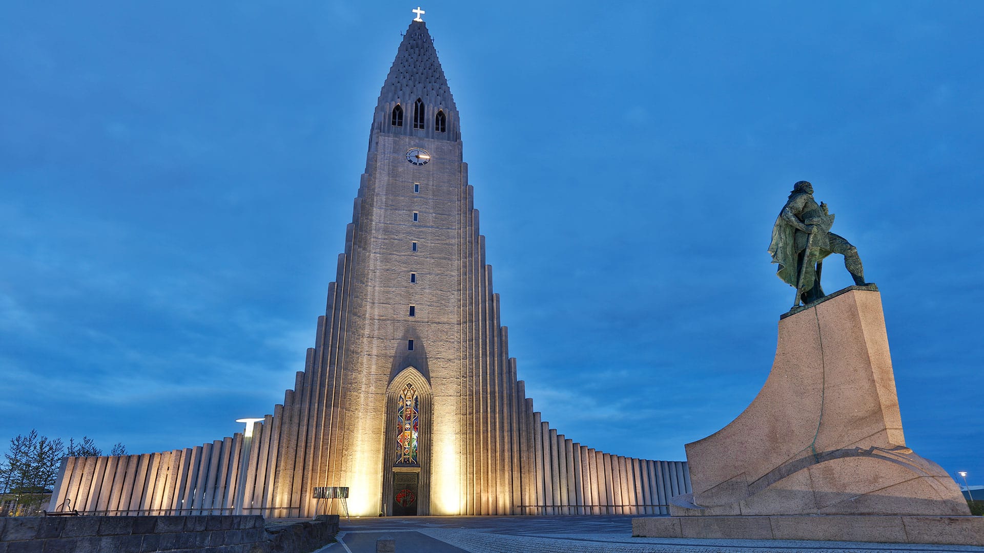 The illuminated Hallgrímskirkja church in Reykjavik, Iceland, with the statue of Leif Erikson in the foreground during dusk.