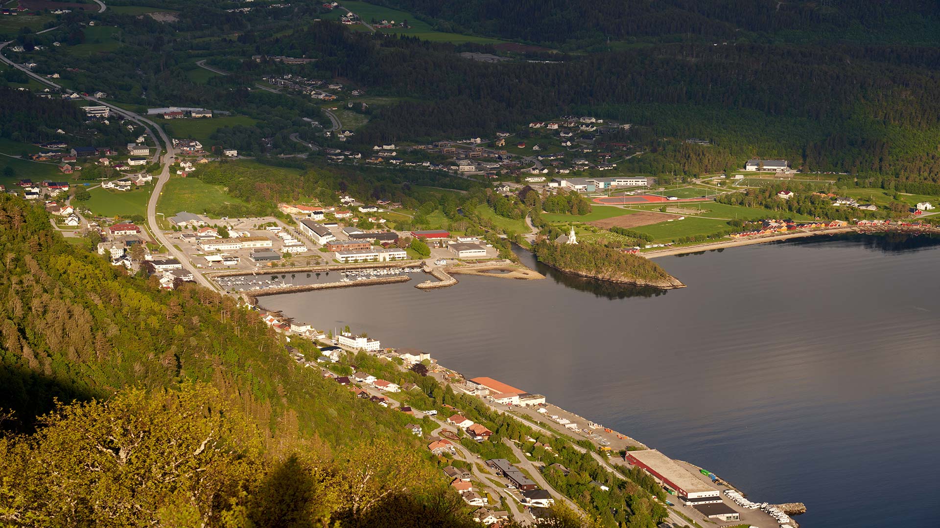 Aerial view of Narvik, Norway, showcasing the harbor, buildings, roads, and green landscape on a sunny day.
