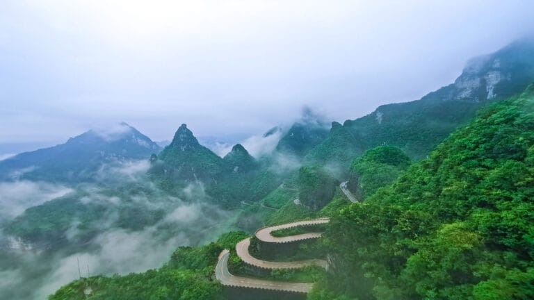 Winding mountain road at Tianmen Mountain surrounded by lush greenery and mist-covered peaks.