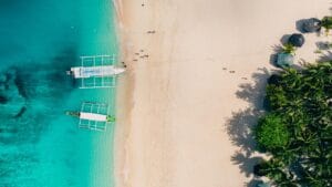 Aerial view of Puka Shell Beach with turquoise waters, boats, and lush greenery in Boracay, Philippines.