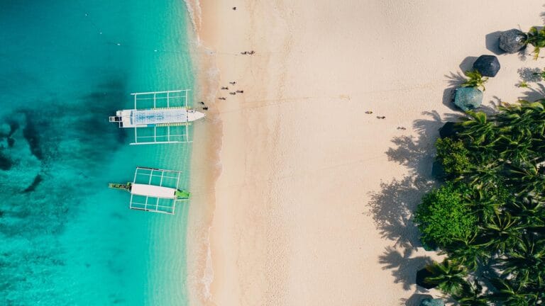 Aerial view of Puka Shell Beach with turquoise waters, boats, and lush greenery in Boracay, Philippines.