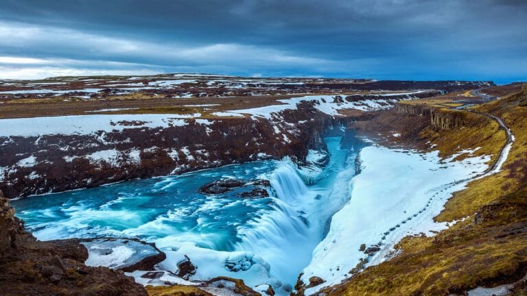 Gullfoss waterfall in Reykjavik, Iceland, during winter with snow-covered cliffs and vibrant blue water.