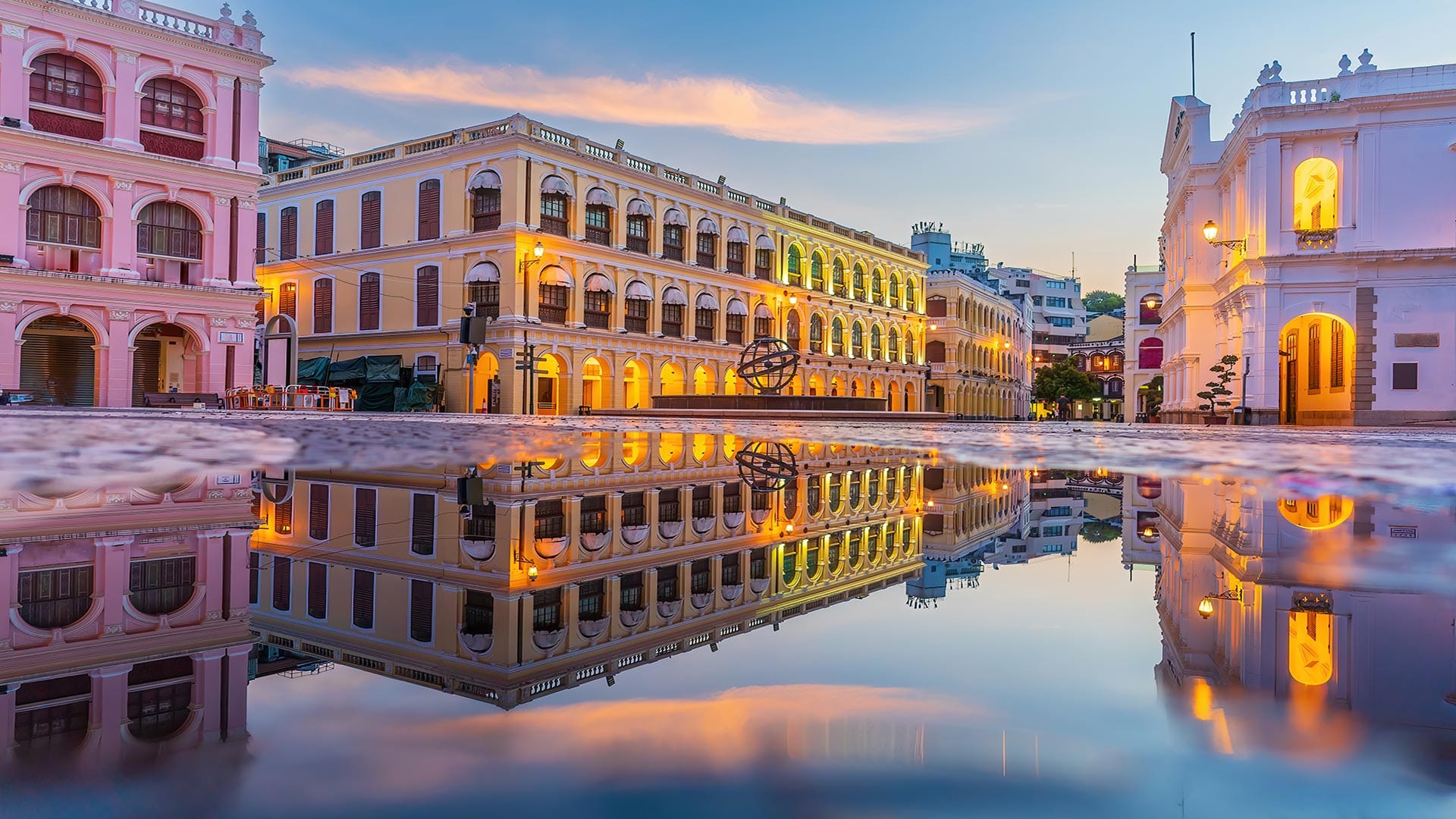 The vibrant and historic Senado Square in Macau, beautifully lit during sunset, reflecting in a puddle for a mirror-like effect.