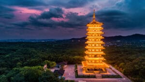 Tam Thai Pagoda illuminated at dusk, surrounded by lush greenery under dramatic skies.