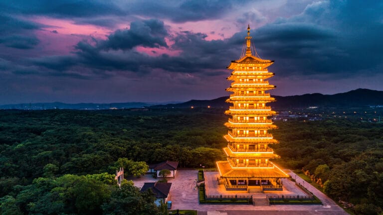 Tam Thai Pagoda illuminated at dusk, surrounded by lush greenery under dramatic skies.