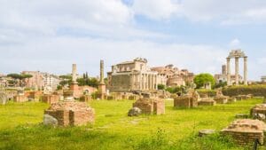 A wide-angle view of the Roman Forum ruins under a bright sky, showcasing ancient columns and buildings.