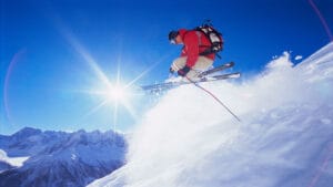 Skier performing a high jump on a snowy slope in South Korea with a bright blue sky